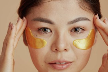 Bej arka planda göz bantları olan genç bir kadın..