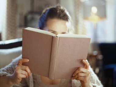 Güneşli kış gününde evde kitap okuyan bir kadına yakın çekim..
