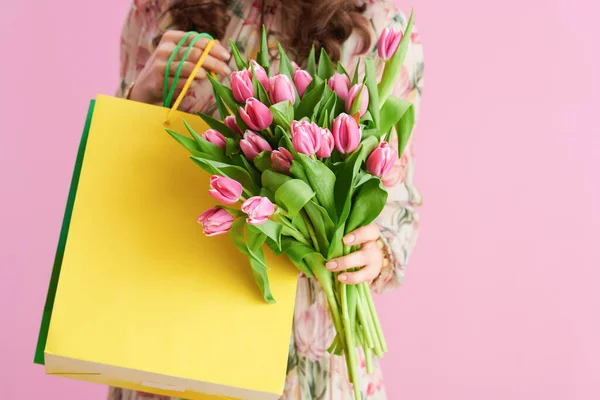 Closeup on woman with tulips bouquet and shopping bags isolated on pink.