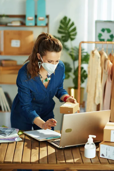 stock image stylish 40 years old small business owner woman with ffp2 mask and an antibacterial agent using laptop in the office.