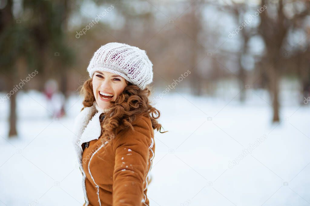 happy stylish woman outdoors in the city park in winter in a knitted hat and sheepskin coat.