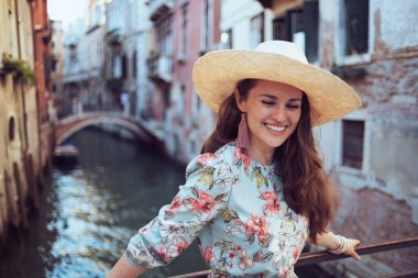 happy elegant middle aged traveller woman in floral dress with hat having walking tour in Venice, Italy.