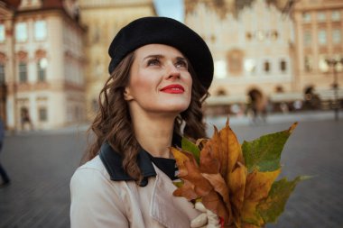 Merhaba sonbahar. Prag 'daki Old Town Meydanı' nda sonbahar sarısı yaprakları olan bej renkli trençkotlu rüya gibi bir kadın..