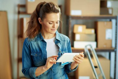 Teslimat işi. Ofiste tablet bilgisayar uygulamaları kullanarak kot giyen modern bir kadın..