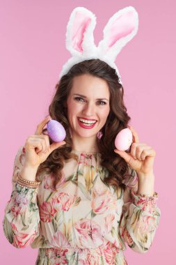 Uzun dalgalı esmer saçlı, tavşan kulaklı ve pembe arka planda paskalya yumurtası olan zarif bir kadın..