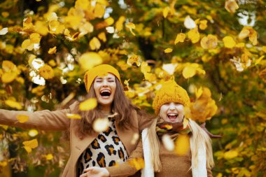 Hello autumn. happy modern mother and child in yellow hats outside in the city park in autumn rejoicing.