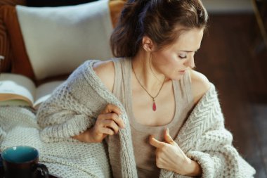 Modern bir sonbahar gününde, modern bir evde modern bir salonda divanın yanında oturan rahat, rahat, rahat bir hırka giymiş modern bir kadın..