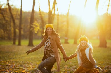 Merhaba sonbahar. Mutlu modern anne ve kız turuncu şapkalı şehir parkında sonbaharda eğleniyorlar..