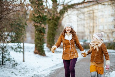 Örgü şapkalı ve koyun derisi ceketli mutlu bir anne ve kız. Örgü şapkalı ve koyun derisi ceketli. Kışları şehir parkında yürüyorlar..