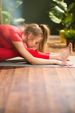 Modern yeşil oturma odasında kırmızı formalı modern kadın yoga yapıyor..