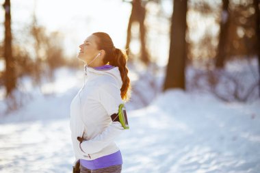 relaxed healthy woman in white jacket with headphones outdoors in the city park in winter.