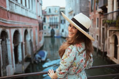 happy stylish solo tourist woman in floral dress with hat sightseeing in Venice, Italy.