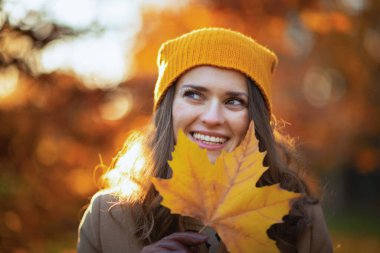 Hello september. happy young woman in brown coat and yellow hat with autumn yellow leaves outside in the city park in autumn.