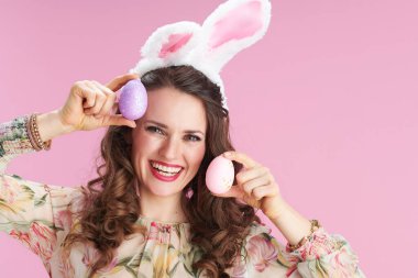 Uzun dalgalı esmer saçlı, tavşan kulaklı ve pembe arka planda paskalya yumurtası olan modern bir kadın..