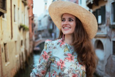 smiling elegant woman in floral dress with hat having walking tour in Venice, Italy.