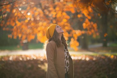 Merhaba Kasım ayı. Sonbaharda şehir parkında kahverengi ceketli ve sarı şapkalı güler yüzlü bir kadın..