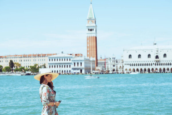relaxed young woman in floral dress with sunglasses and hat having walking tour on San Giorgio Maggiore island.
