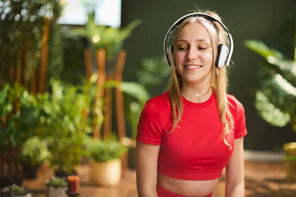 Onnellista Modernia Naista Punaisissa Kuntoiluvaatteissa Kuuntelemassa Musiikkia Kuulokkeilla Modernissa Vihreässä — kuvapankkivalokuva