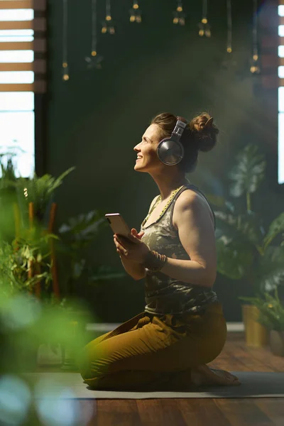modern woman with smartphone listening to the music with headphones in the modern green house.