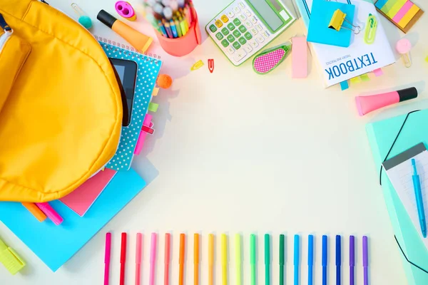 Back to school. Upper view of white desk with workbooks, stationary, backpack and coloured markers at student room in sunny day.