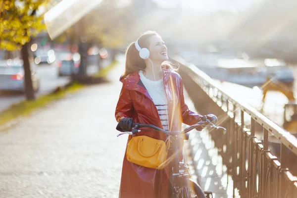 Улыбающаяся Современная Женщина Красном Дождевике Велосипедом Наушниками Улице Города — стоковое фото