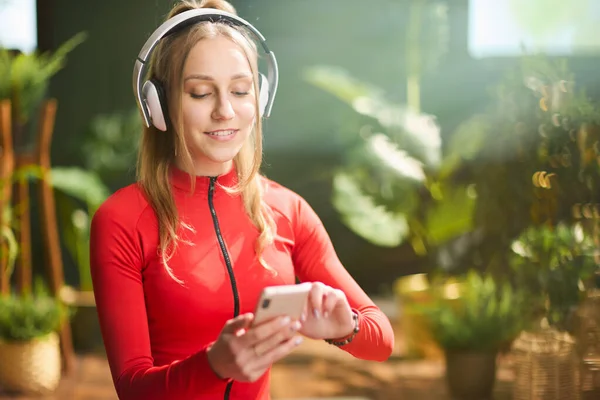 Glimlachende Jonge Vrouw Rode Fitnesskleding Met Hoofdtelefoon Met Smartphone Modern — Stockfoto