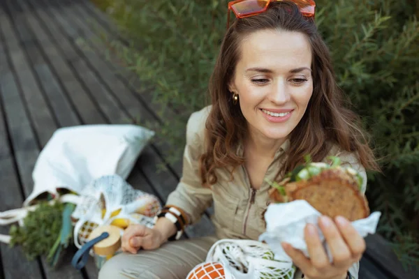 Smiling Stylish Woman Overall Tote Bag String Bag Sandwich Sitting — Stockfoto