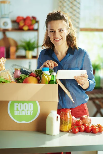 Food delivery. happy modern woman with food box using tablet PC app in the kitchen.