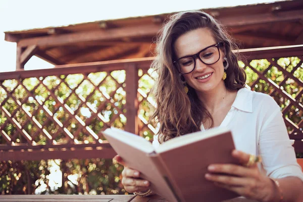 Smiling Modern Woman White Shirt Eyeglasses Sitting Table Reading Book — Stockfoto