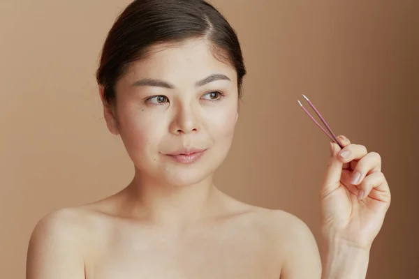 young asian female with tweezers on beige background.