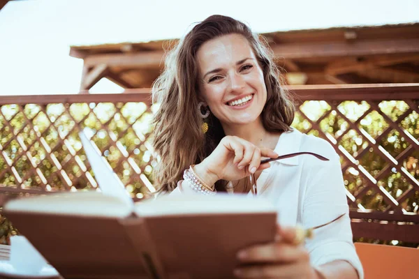 Portrait Smiling Modern Woman White Shirt Eyeglasses Sitting Table Reading — Φωτογραφία Αρχείου