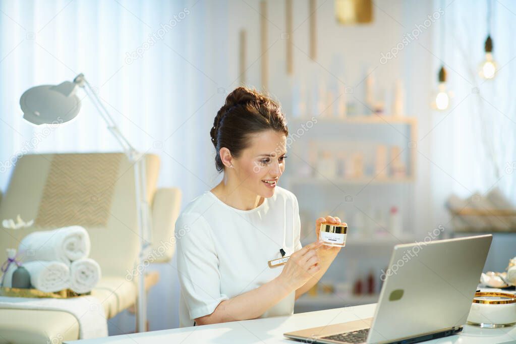 smiling 40 years old woman employee with laptop having video meeting in modern beauty studio.