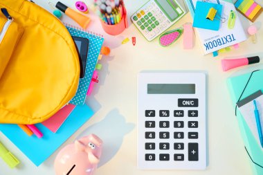 Okula dönelim. Çalışma kitapları, sabit, ders kitabı, hesap makinesi ve sırt çantası olan beyaz masanın üst görünümü güneşli bir günde okul çocuk odasında.