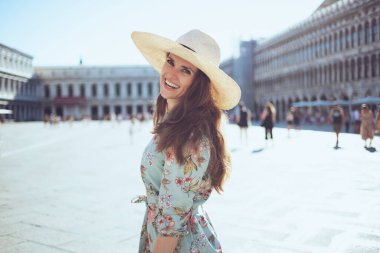 happy young traveller woman in floral dress with hat sightseeing at Piazza San Marco in Venice, Italy.