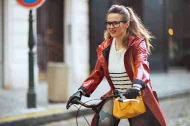 Kırmızı yağmurluklu şık bir kadın şehirde bisiklet sürüyor..