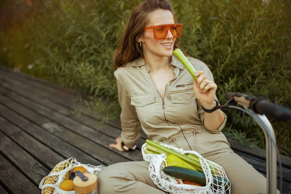 Smiling Modern Woman Sunglasses Overall String Bag Scooter Celery Eating — 图库照片