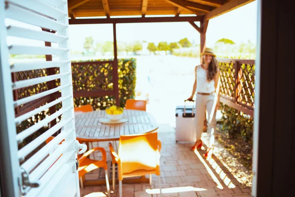 Closeup on door and woman with wheel bag in background in the patio of hotel guest house in the terrace.