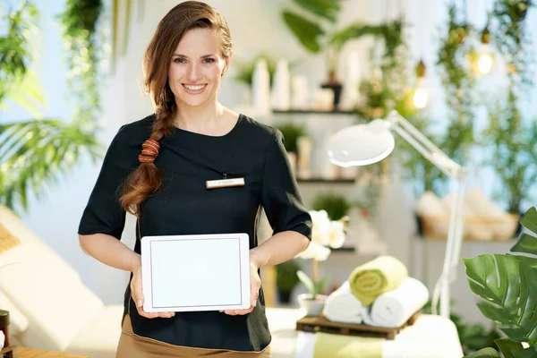 happy 40 years old woman employee in modern beauty studio showing tablet PC blank screen.