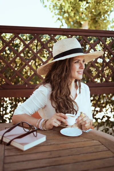 Relaxed Modern Female White Shirt Book Hat Eyeglasses Sitting Table — Stock fotografie