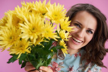 Mutlu modern 40 yaşındaki kadın portresi, uzun dalgalı esmer saçlı, sarı kasımpatı çiçekli pembe arka planda izole edilmiş..