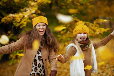 Hello october. happy modern mother and daughter in orange hats outdoors on the city park in autumn rejoicing.