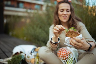 Şehirde dışarıda otururken, elinde ip torbası ve sandviçle gezen mutlu kadına yaklaş..