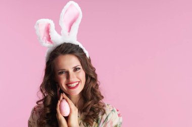 Uzun dalgalı esmer saçlı, tavşan kulaklı ve pembe arka planda paskalya yumurtası olan genç bir kadın..