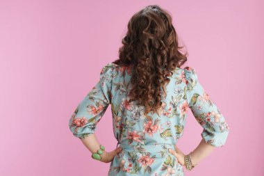 Arkasında pembe arka planda bilezikleri olan çiçekli elbiseli bir kadın var..