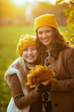 Hello september. smiling young mother and child in orange hats with autumn yellow leaves outside in the city park in autumn.