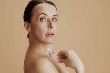 Modern orta yaşlı kadın tekerlekli masaj aleti ile bej arka planda izole edildi.