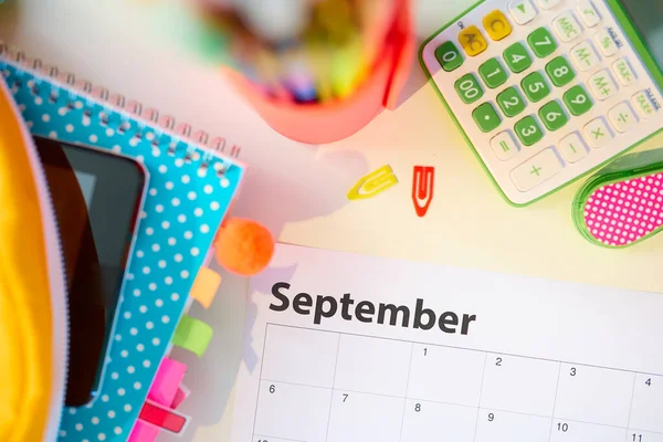 Back to school. Upper view of white table with workbooks, stationary and september calendar at school child room in sunny day.