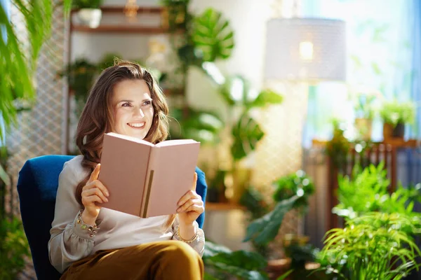Green Home. happy stylish housewife with long wavy hair with book at modern home in sunny day.