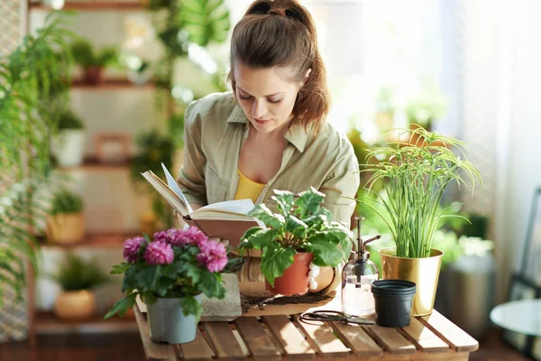 Relaxing home gardening. young housewife in white rubber gloves with potted plant and book at modern home in sunny day.