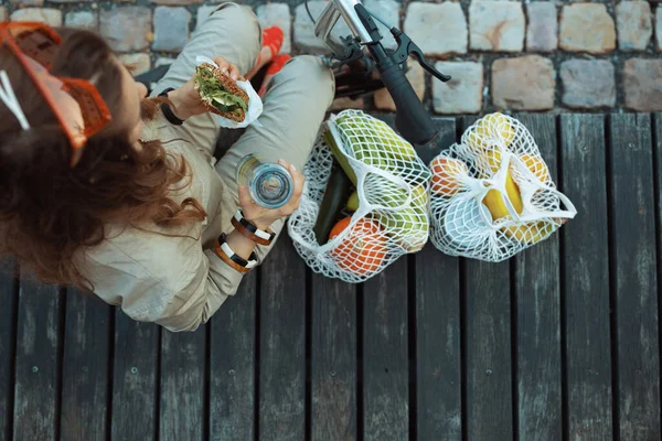 在城市里 女人坐在外面吃饭时 总体上看是用绳子包 滑板车 水瓶和三明治的上层形象 — 图库照片